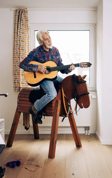 子供部屋でカウボーイを果たしている高齢者の屋内肖像画 木製の馬に座って ストック画像