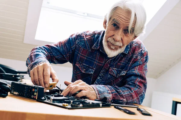 机に座っている老人の屋内肖像画 彼のマザーボードにCpuを差し込みます ロイヤリティフリーのストック写真
