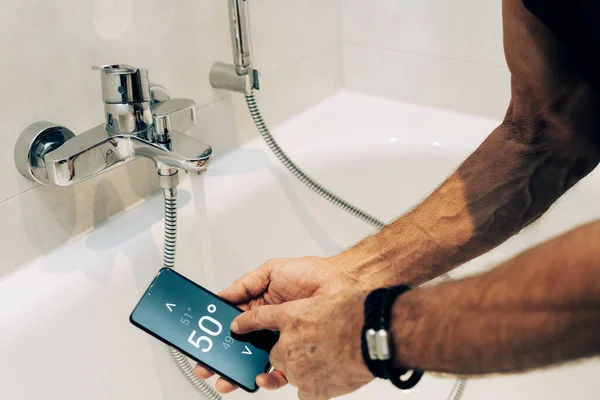 スマートホーム概念 男は彼の携帯電話上のアプリを使用して温水温度を制御します ストック画像