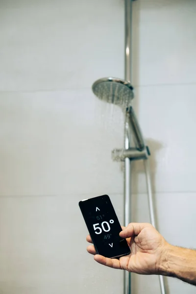 スマートホーム概念 男は彼の携帯電話上のアプリを使用して温水温度を制御します ロイヤリティフリーのストック画像