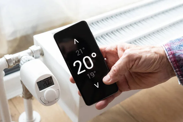 スマートホームコンセプト 携帯電話上のアプリを使用して加熱温度を制御する男 ストック写真