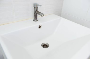 The ceramic sink basin with the stained faucet near the white tile wall of the restroom in the city house, front view with the copy space.