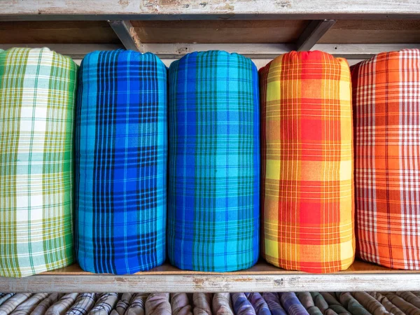 The handmade woven silk rolls with the plaid pattern are on shelves inside a local clothing store in Thailand, front view with the copy space.