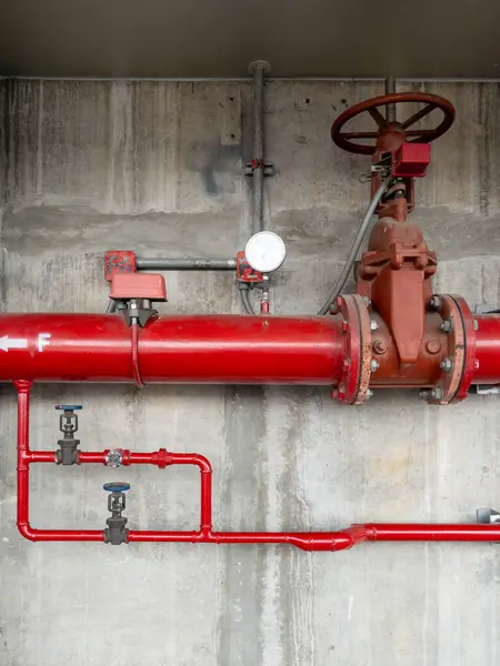 The large valve on the red metal pipe of the fire fighting system near the concrete wall of the train station in the city, front view for the copy space.