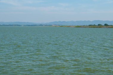 Dağ sıraları arasındaki düzlüklerde bulunan büyük rezervuarın baraj sırtı boyunca uzanan asfalt yolun görüntüsü, fotokopi alanı ile ön manzara.