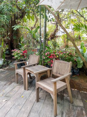 Tahta sandalye ve masa, tropikal bahçenin yakınındaki ahşap zeminde rahatlamak için kurulmuş, fotokopi alanı için ön manzara..