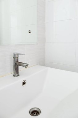 Beyaz seramik lavabo lavabosundaki lekeli musluk şehir evindeki tuvaletin beyaz fayans duvarının yanında. Arka plan için ön manzara..