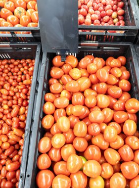 Bir süpermarkette siyah plastik sepetlere yerleştirilmiş taze, olgun domateslerin yakın plan görüntüsü. Bu canlı kırmızı sebzeler yemek, salata ve süslemeler için idealdir. Tazelik ve kaliteyi yansıtır..