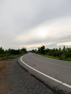 Huzurlu bir kırsal alanda kıvrımlı düzgün asfalt bir yol, sulama kanalına paralel gidiyor, fotokopi alanı ile ön manzara. 