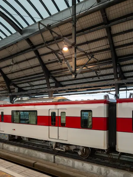 Modern bir banliyö treni hareketli bir istasyon platformunda dinleniyor. Kırmızı ve beyaz dış görünüşü, kemerli çatının altında şehir yolcuları için parlıyor..