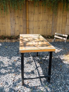 Eski bir kapıdan yapılmış bir ahşap masa bambu ve yemyeşil ağaçlarla çerçevelenmiş eski bir bahçe kafesinde taş bir verandayı süslüyor. Sakin bir kaçış için ideal..