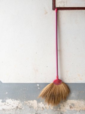 Eski bir süpürge ahşap sapı ve saman kılları ile solmuş bir kırsal ev duvarında asılı, geleneksel temizlik aletleri depolama