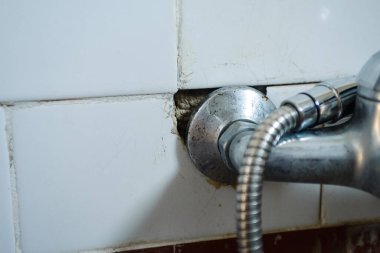 Duvara monte edilmiş eski duş musluğu. Banyoda koyu kırmızı ve beyaz fayanslar var.