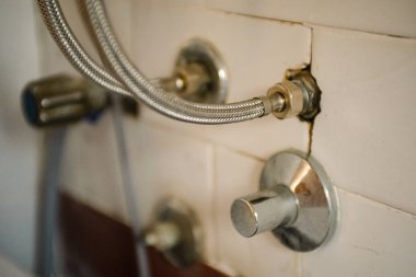 Kapakçıklı eski tesisatlar, su girişi ve banyodaki kırmızı ve beyaz fayanslı priz.