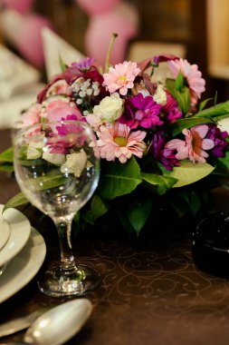 Servis masasının üzerinde boş bir şarap kadehi. Yanında da süs olarak bir buket çiçek var.