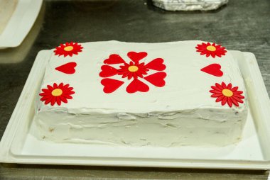 Kalp ve çiçek şeklinde kırmızı yenilebilir süslemelerle süslenmiş beyaz doğum günü pastası