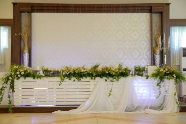 Beyaz tüyle süslenmiş beyaz gelinlik masası ve yeşil ağaçlarla süslenmiş çeşitli çiçekler.