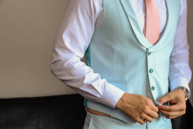 Pembe kravatlı bir adam mavi yeleğini resmi bir şekilde ilikliyor.