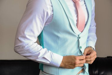 Pembe kravatlı bir adam mavi yeleğini resmi bir şekilde ilikliyor.