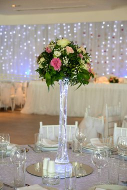 Bir buket çiçek cam vazoda düğün salonundaki masanın üstünde bir süs olarak duruyor.