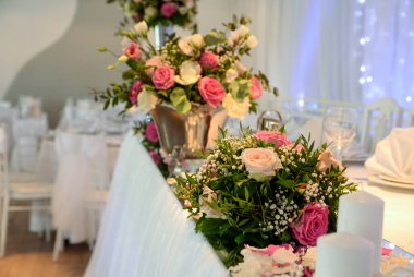 Çiçek buketleri, beyaz mumlar ve dağınık taç yaprakları bir düğünde sofra süsü olarak kullanılıyor.