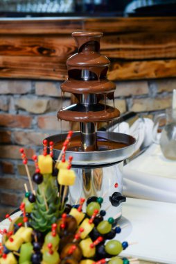 Düğün pastası olan servis masası, çikolata çeşmesi, meyve süslemeleri ve çeşitli renklerde küçük pastalar..