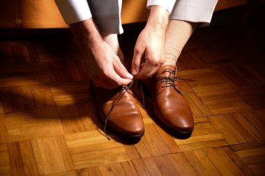 Bir adam kahverengi ayakkabısının bağcıklarını odadaki zavallılara bağlıyor.