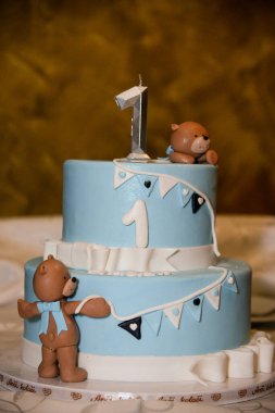 Mavi yuvarlak, üzerinde oyuncak ayılar olan iki katlı doğum günü pastası, üstünde bir numara ve erkek adı Lazar.