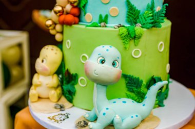 Dinozorlarla dolu iki katlı bir doğum günü pastası ve üzerinde Matej yazan renkli süslemeler..