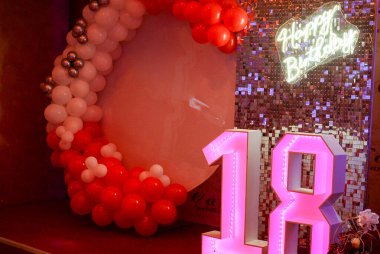 Kırmızı ve beyaz balonlar neon ışıklarla süsleme amaçlı, ve bunun da yardımıyla mutlu yıllar ve ayrıca pembe ışıkla aydınlatılmış 18 numara.