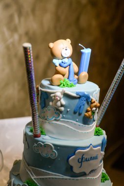 Üç katlı mavi beyaz bir doğum günü pastası, ayı şeklinde heykelcikler ve Kiril alfabesiyle yazılmış erkek isimli bir tavşan..