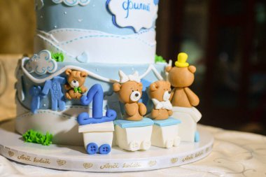 Üç katlı mavi beyaz bir doğum günü pastası, ayı şeklinde heykelcikler ve Kiril alfabesiyle yazılmış erkek isimli bir tavşan..