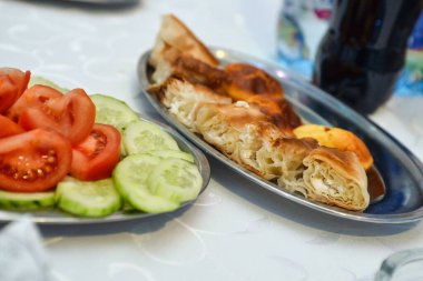 Bir tabakta domates ve salatalık salatası diğerinde de peynirli çıtır ev yapımı turta var. Servis edildi..