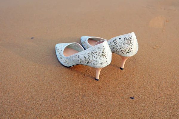 Women\'s white high heels on the wet beach