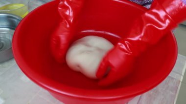 Şef bir restoranda kırmızı plastik kasede hamur yoğuruyor.