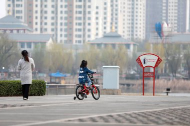 LUANNAN COUNTY, Hebei Eyaleti, Çin - 24 Mart 2020: Küçük bir kız bisiklete binmeyi öğreniyor, maske takarak koronavirüs zatürreesini koruyor