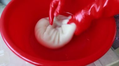 Şef bir restoranda kırmızı plastik kasede hamur yoğuruyor.