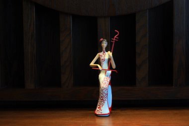 Cheongsam gibi giyinmiş ve müzik aletlerini kucaklayan bir figür.