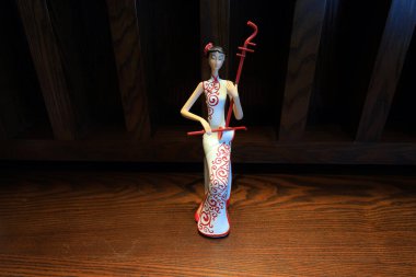 Cheongsam gibi giyinmiş ve müzik aletlerini kucaklayan bir figür.