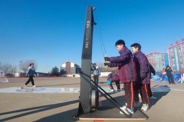 LUANNAN COUNTY, China - December 24, 2021: Students are experiencing wind resistance to simulate a ski on the playground, North China. clipart