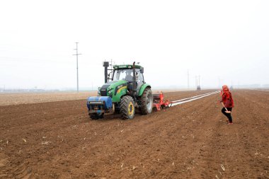 LUANNAN COUNTY, Hebei Eyaleti, Çin - 2 Nisan 2021: Çiftçiler ekicileri çiftliğe plastik mısır ekmeleri için sürüyorlar