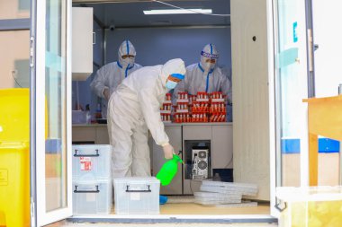 LUANNAN COUNTY, Çin - 29 Mart 2022: Tıbbi tecrit giysileri içinde tıbbi işçiler Kuzey Çin 'deki nükleik asit test örneklerinin nakil kutusunu dezenfekte ediyorlar