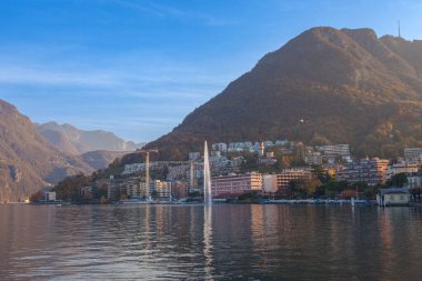 Lugano, İsviçre - 12 Kasım 2021: Otel ve fıskiyeli kıyı gölünde sonbahar günbatımı