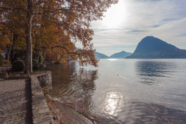 Lugano Gölü 'nde sonbahar gündoğumu, San Salvatore ve San Giorgio tepeleri ve İsviçre' nin arka planında sonbahar renklerinde ağaçlarla birlikte. Dinginlik ve rahatlama kavramı