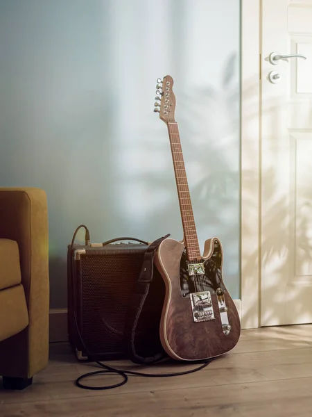电吉他和扩音器站在沙发和门窗之间的地板上 沐浴在阳光下 — 图库照片