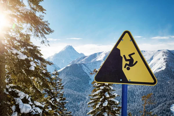 Yellow warning sign on the edge of the ski slope in mountains