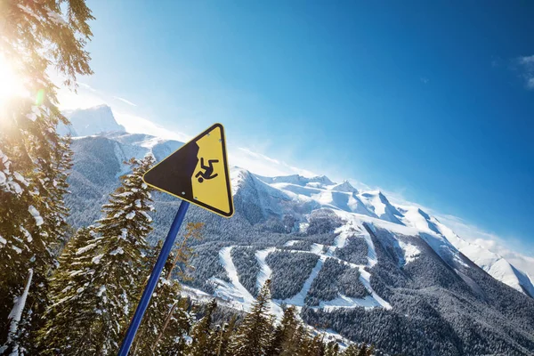 Yellow warning sign at a ski resort, ski slopes in the background