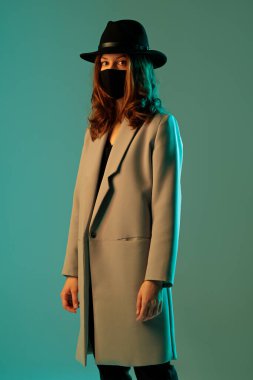 Yeşil arkaplanlı, şapkalı ve koruyucu maskeli şık bir kadın..