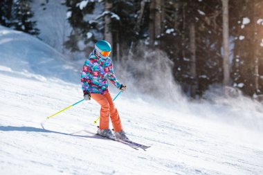 Parlak elbiseli genç kayakçı güneşli bir günde yamaçtan aşağı kayıyor..