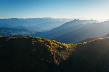 Altın güneş ışığı dağlık bir yamaçta sonbahar yapraklarını vurgular, uzak dağ zirveleri yumuşak mavi sise dönüşür, Georgia.